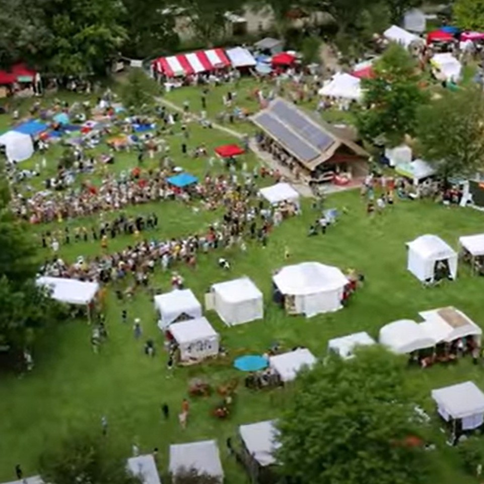Toma aérea de un festival, mostrando carpas blancas y una multitud de personas celebrando.