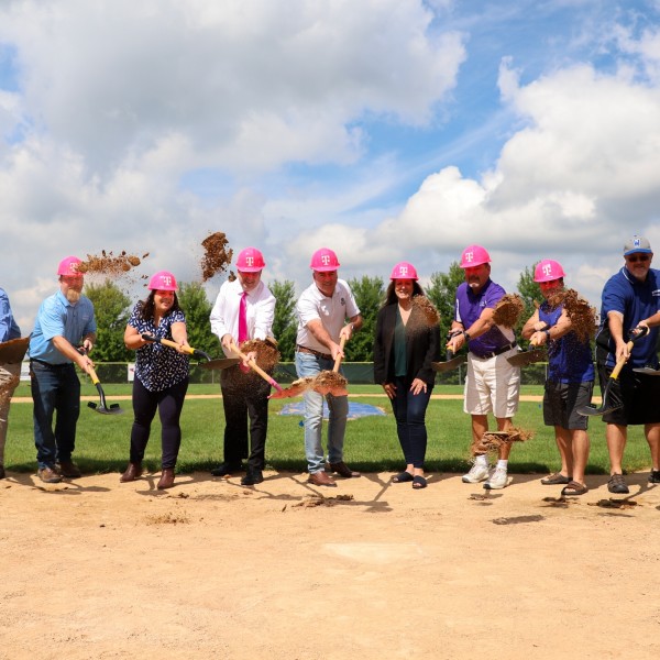 A group of people wearing T-Mobile branded hard hats and holding shovels gather on a baseball field.
