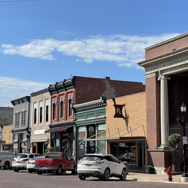 Photo of a downtown scene showing historic storefronts and a line of parked cars.