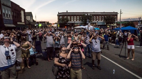 Una multitud se reúne en el centro de Sweetwater, Tennessee, para ver el eclipse solar total de 2017. Todos llevan gafas protectoras y miran hacia el cielo.