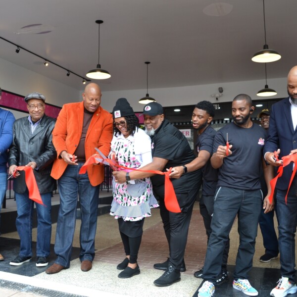 A group of people cutting a large red ribbon at the grand opening of a small business
