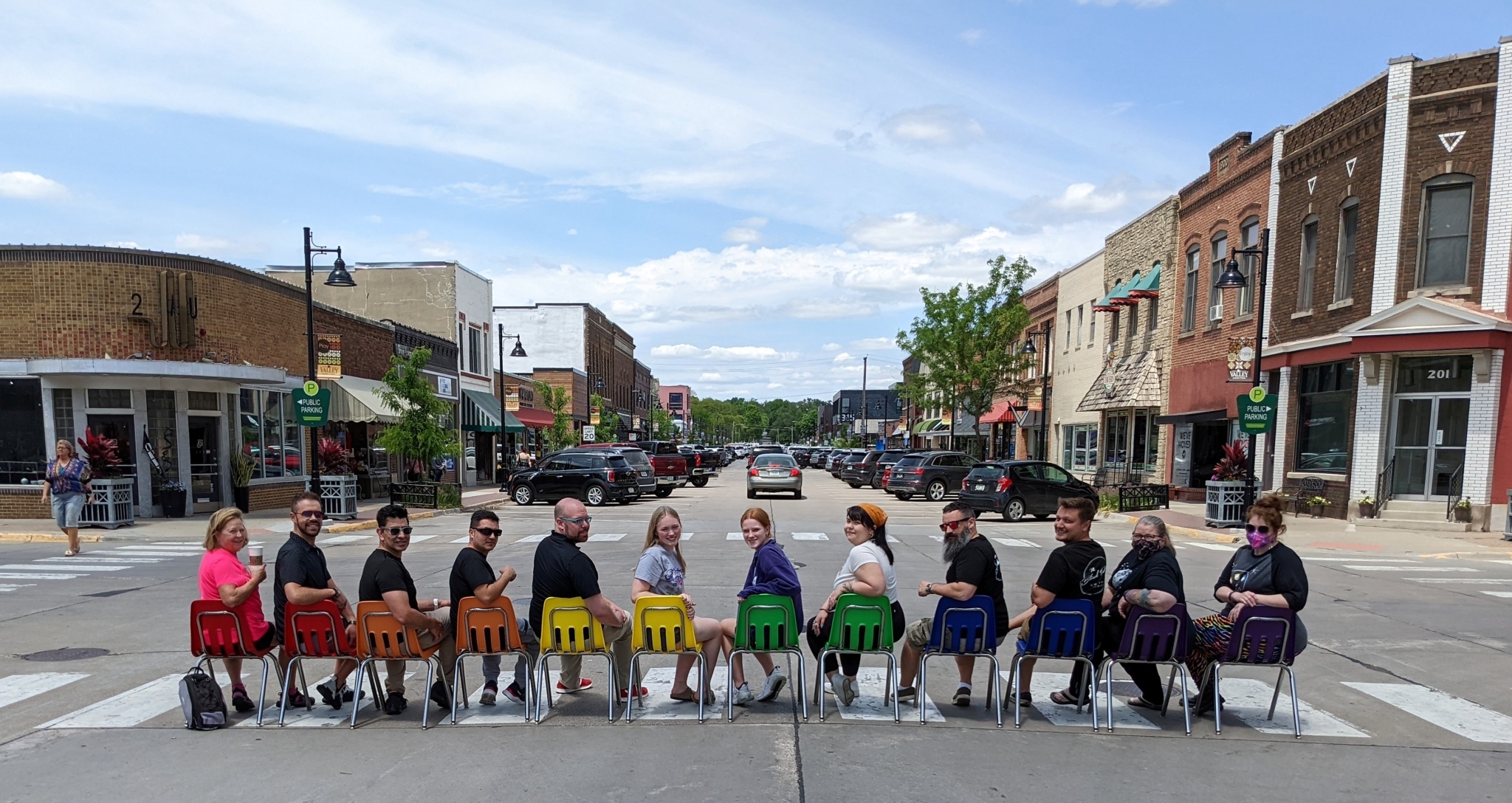 Community members in Downtown Valley Junction in West Des Moines, Iowa celebrate Pride Month sitting in colorful chairs