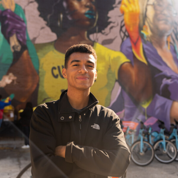 Hombre de pie delante de un mural de colores y bicicletas con los brazos cruzados.