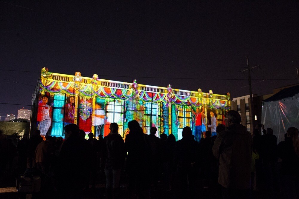 A large group of people gather in front of an brightly illuminated building at night.