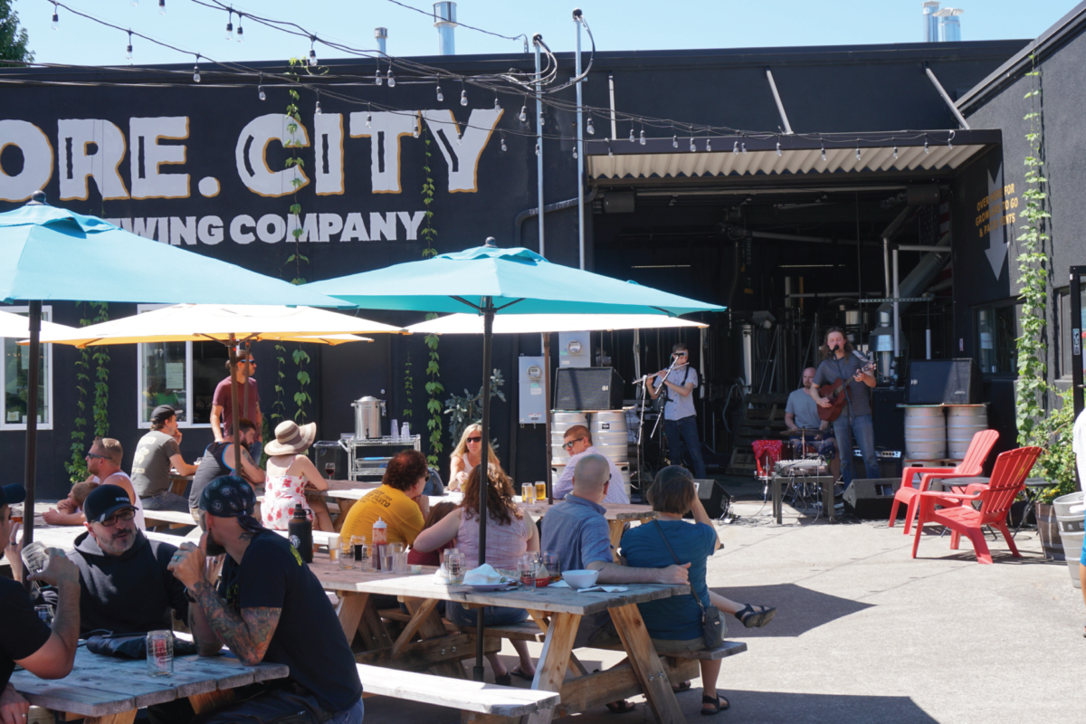 En un día soleado, la gente se reúne en las mesas de picnic al aire libre de una cervecería.