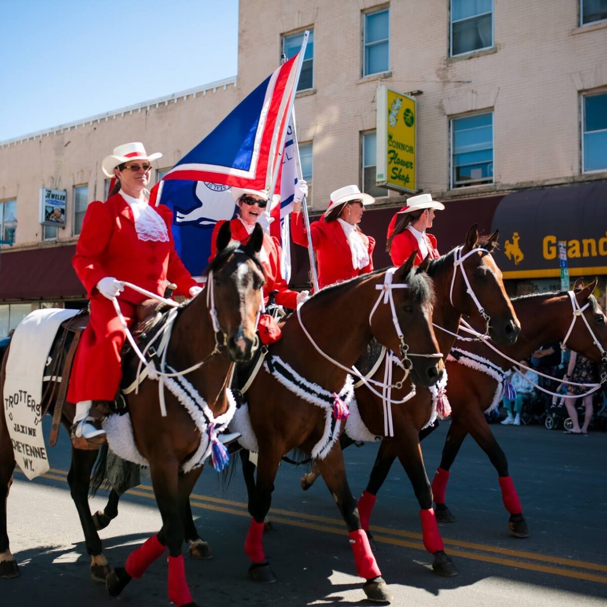 Four women dressed in bright red, ceremonial Western attire ride horses down Main Street.