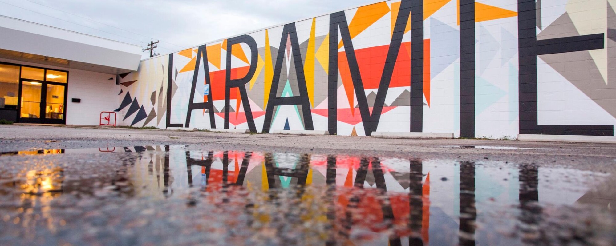 Mural con la palabra "LARAMIE" reflejada en el charco de un aparcamiento.
