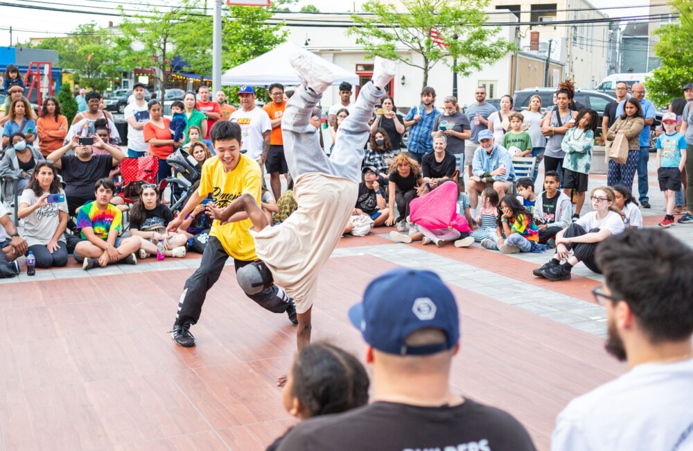 Espectadores de todas las edades se reúnen en torno a una pista de baile al aire libre para animar a dos chicos que bailan breakdance.