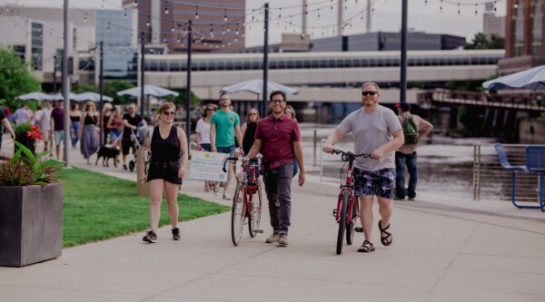 Pedestrians, some walking bikes and with dogs, stroll down a well designed riverfront sidewalk.