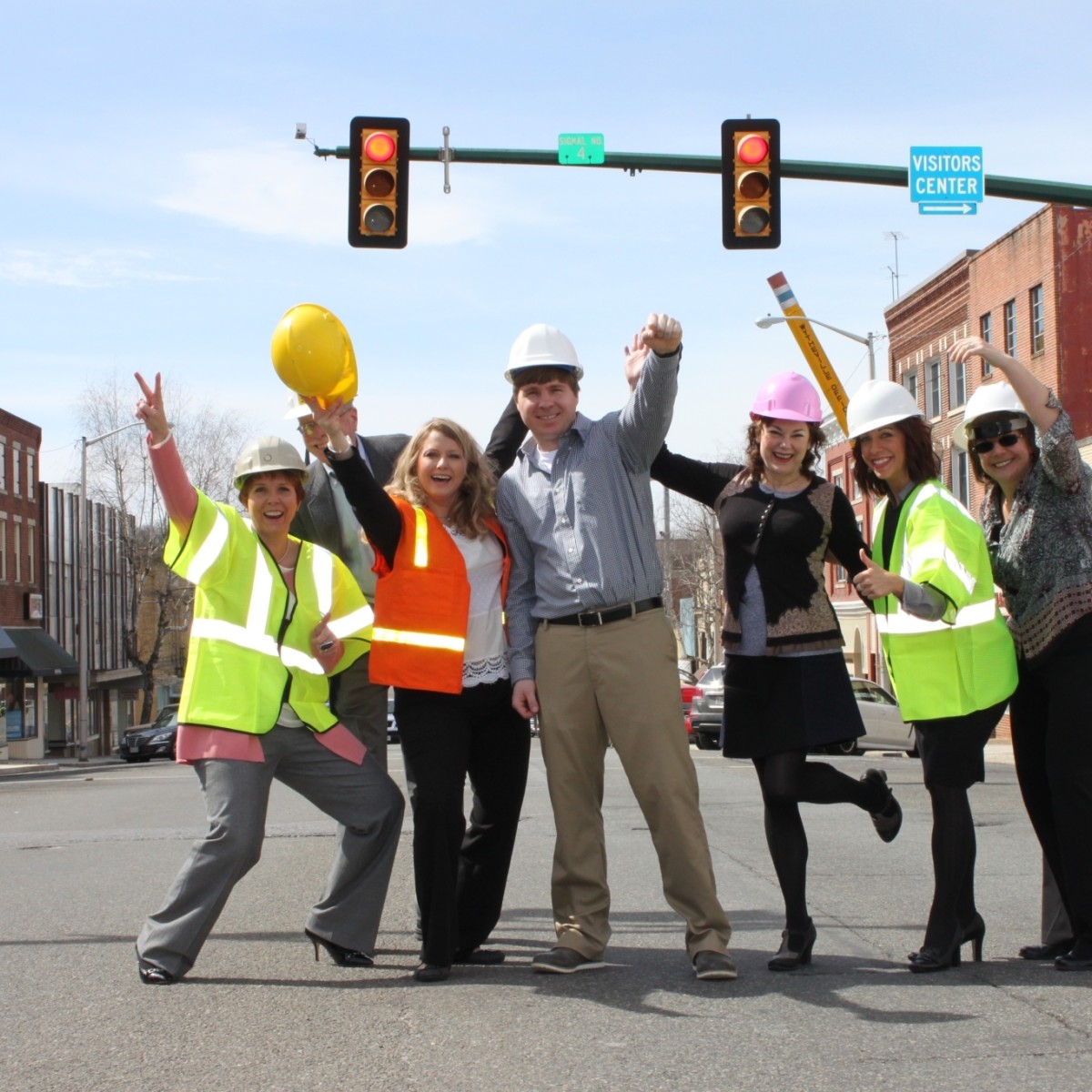 A small group of people wearing hi-vis vests and hard hats stand in the middle of an intersection celebrating the kick-off of streetscape improvement project.