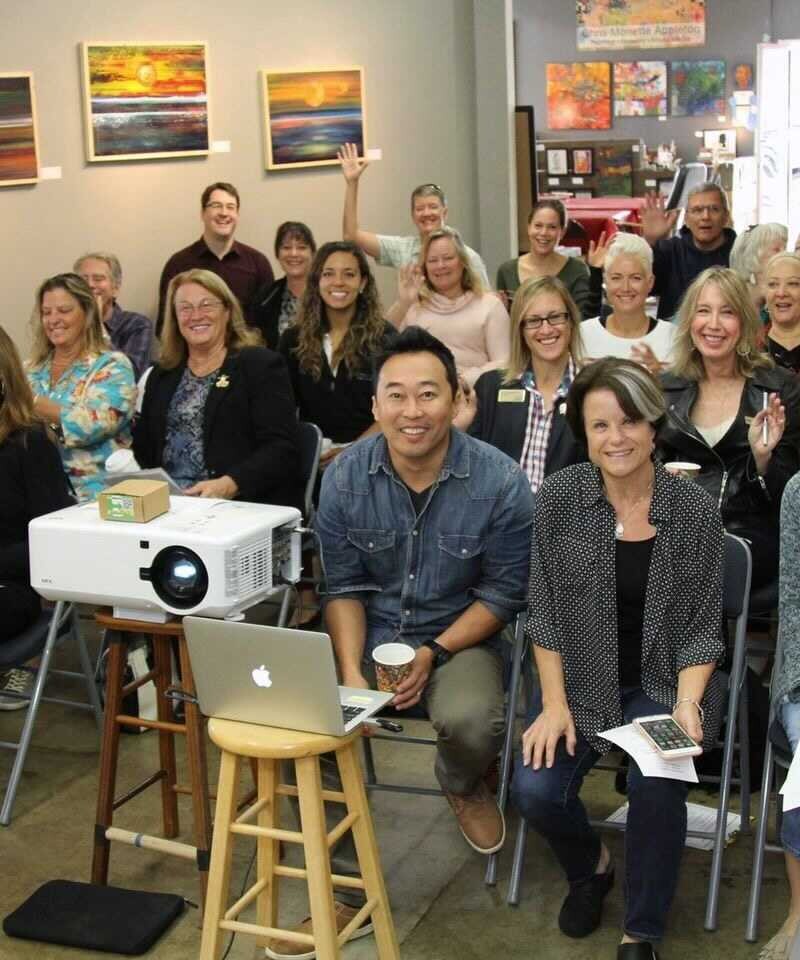 Gran grupo de personas reunidas en una oficina sonriendo a la cámara delante de un proyector.
