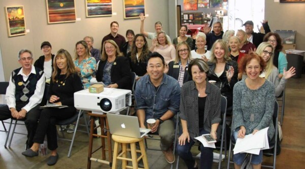 Gran grupo de personas reunidas en una oficina sonriendo a la cámara delante de un proyector.