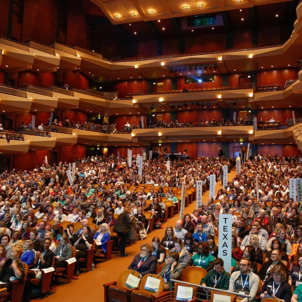 Más de 1.000 personas se reúnen en un gran auditorio con butacas de teatro y de palco; algunas sostienen carteles con los nombres de los estados de Estados Unidos.