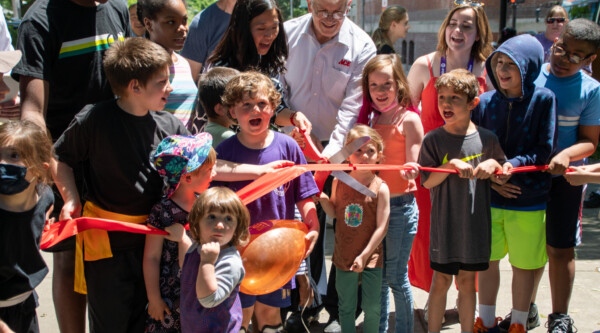 Children and adults participate in a ceremonial ribbon cutting.