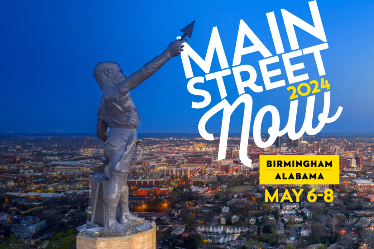 Estatua de Vulcano con el horizonte iluminado de la ciudad de Birmingham al fondo. La lanza alzada de la estatua señala el logotipo de Main Street Now 2024 en la esquina superior derecha.