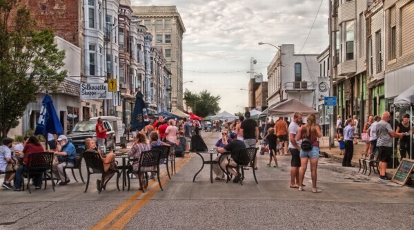 People gathering around tables and in groups at an open streets event.