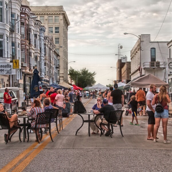 People gathering around tables and in groups at an open streets event.
