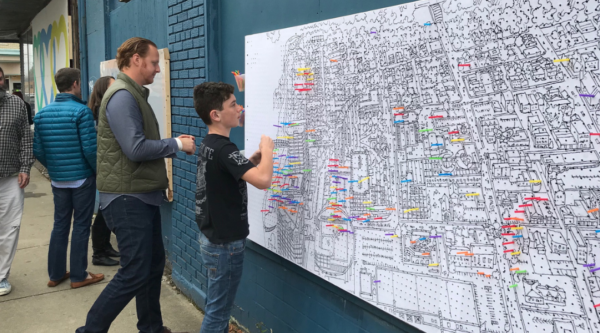 Un grupo de personas añade chinchetas de colores a un mapa del centro de la ciudad durante un ejercicio de planificación comunitaria.