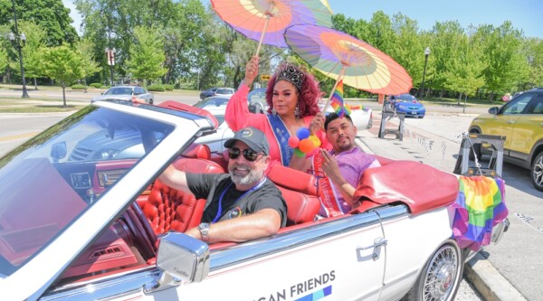 Evento del orgullo de Waukegan, personas con atuendos arco iris montadas en un coche durante un desfile.