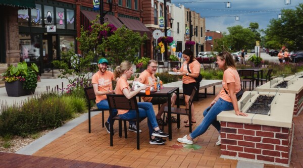 Personas con camisetas de Uptown Marion se reúnen alrededor de una mesa en el centro de Marion, Iowa.