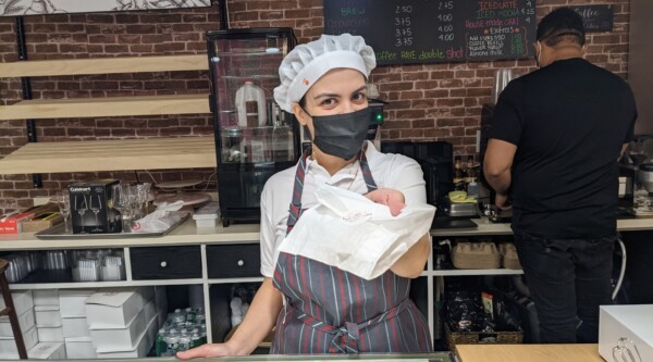 A woman in a chef hat and apron hands a pastry over a counter