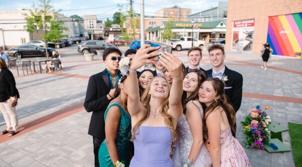 A group of teens in prom dresses poses for a selfie