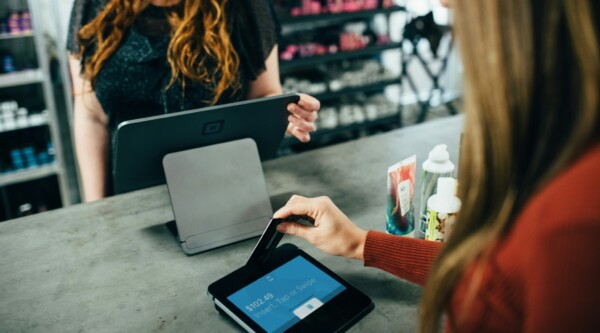 Una mujer frente a una caja registradora mientras otra introduce su tarjeta de crédito en una máquina de pago.