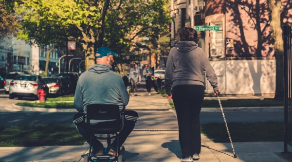 A person using a wheelchair and a person using a cane walk down a sidewalk in Chicago, Illinois.