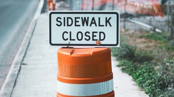 Orange cone holding a sign that says "sidewalk closed"