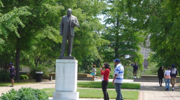 People stroll through a beautifully landscaped park while a man and woman pause to visit a bronze statue of Martin Luther King, Jr.