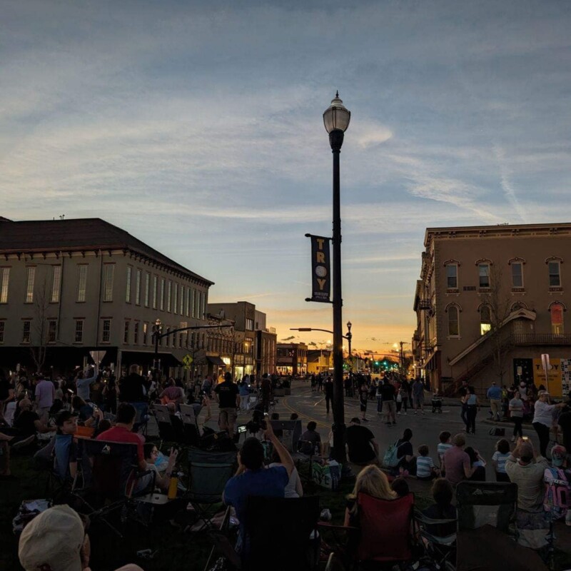 People sitting under a darkened sky on a historic Main Street look up at the eclipse