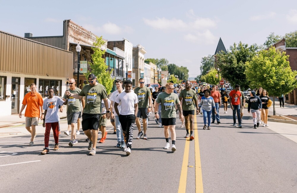 A large group of youth and adults walk down a Main Street.