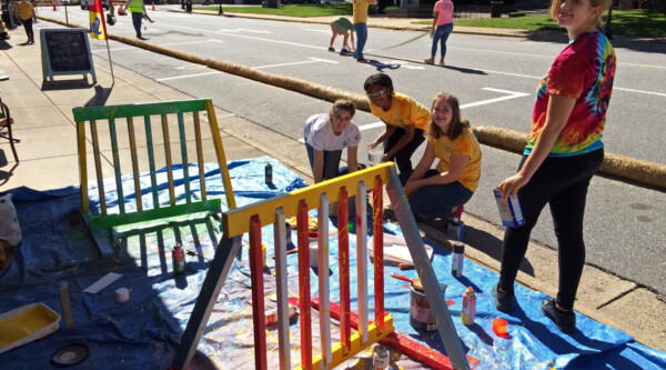 A group of young people paint bike racks on a city street while smiling at the camera.