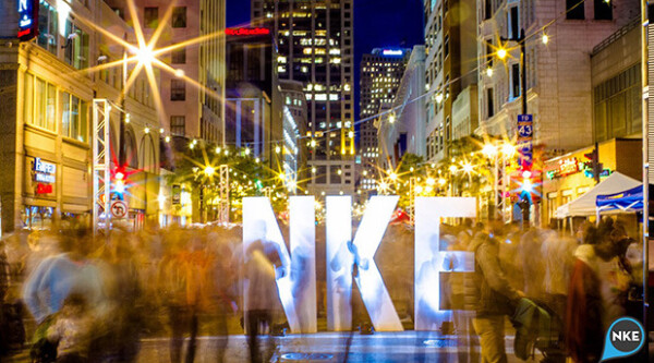 Escena nocturna en corredor comercial urbano entre la multitud, con letras; "NKE" en la calle
