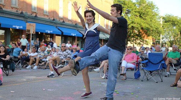 A man and a woman swing dance in 1940s costumes at a downtown festival