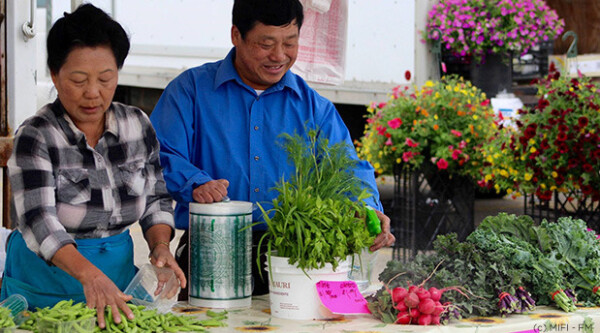 A man and woman sell flowers at a farmers market stall.