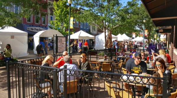 Outdoor downtown scene with large crowd exploring white tents with food vendors and outdoor dining.