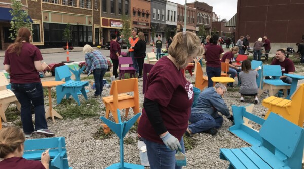 Group of volunteers paint benches in an empty lot in a downtown district.