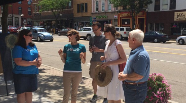 A small group of people talk on a downtown street. Patrice tours Downtown Howell, Michigan, with Howell Main Street Executive Director Cathleen Edgerly, staff, and Howell Mayor Proctor.