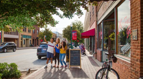 Grupo de tres jóvenes se toman un selfie delante de un negocio del centro de la ciudad.