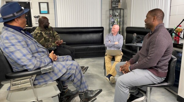 Un grupo de cuatro hombres se sientan en círculo a hablar en una barbería.