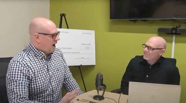 Dos hombres profesionales se sientan en un despacho delante de un micrófono.