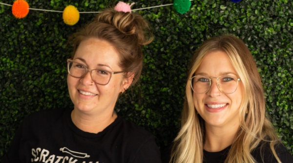 Dos mujeres sonrientes con camisetas negras en las que se lee "Scratch Made Bakery".