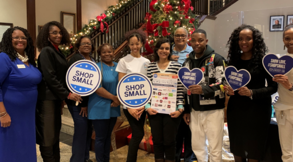 A group of people pose in front of a Christmas tree holding "Shop Small" signs