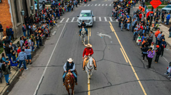 Men ride horses down a street while crowds watch from either side