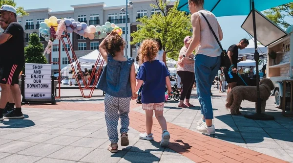 Two children holding hands walking around a spring festival in a downtown plaza