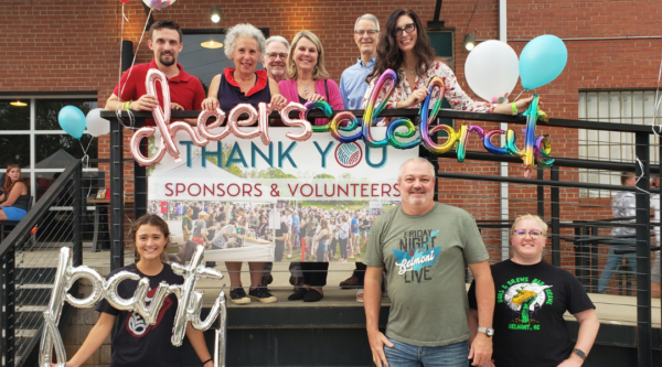 Belmont Main Street's volunteer gather for a celebration and pose holding balloons and a banner