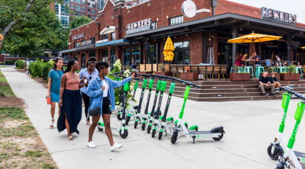 Young women walk past parked e-scooters in Charlotte, N.C.