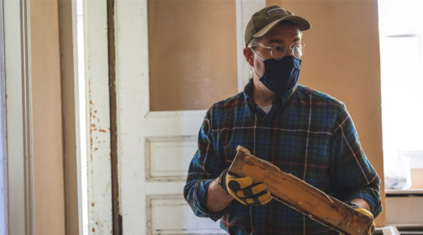 Un hombre sostiene un trozo de madera histórica mientras imparte una clase sobre recuperación de madera.