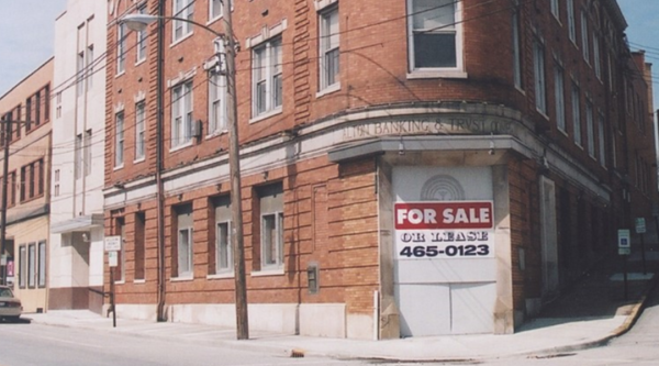 Edificio esquinero de ladrillo en forma de cuña con un cartel de se vende